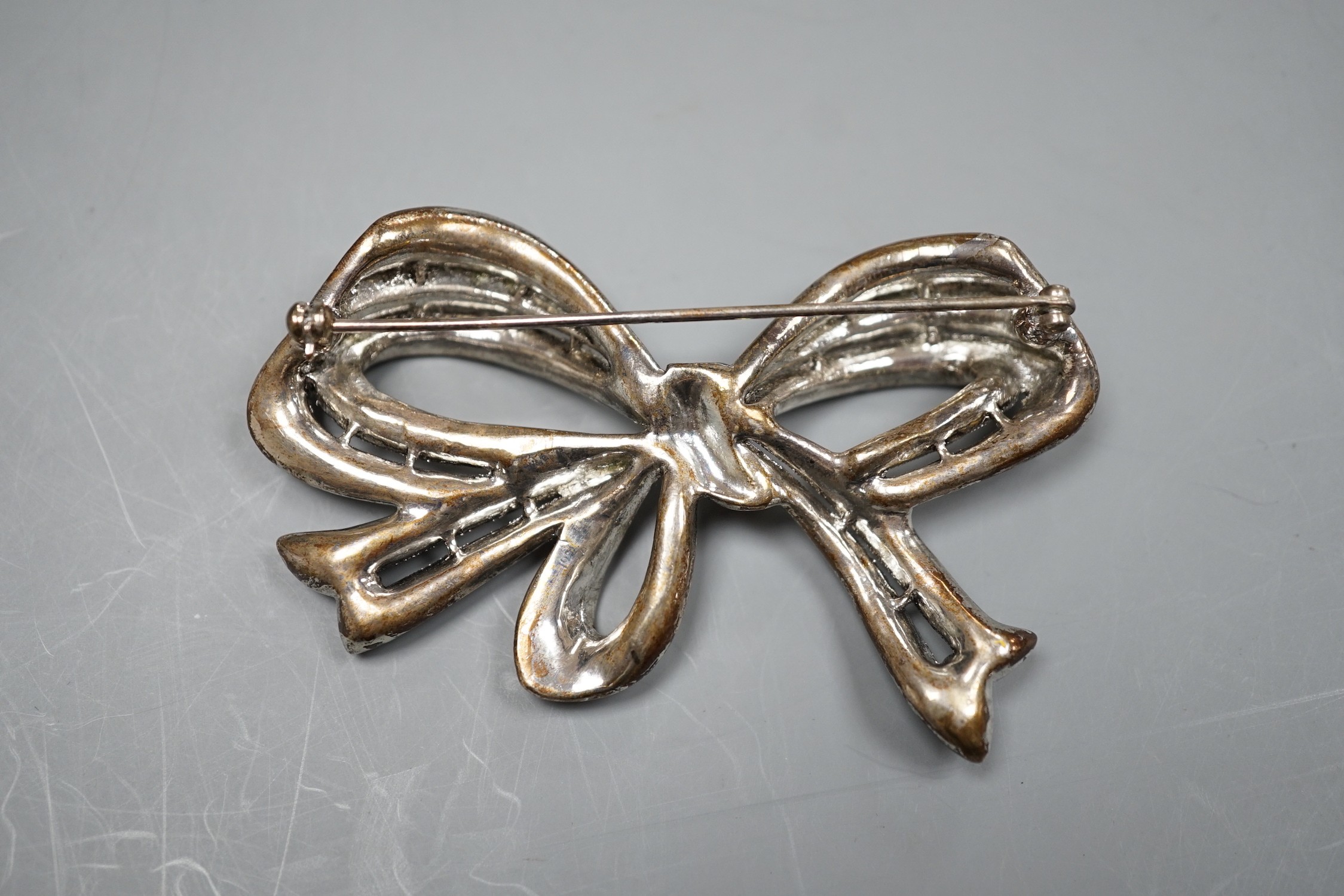 A white metal and paste set ribbon bow brooch, 77mm.